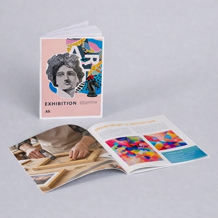 Two art exhibition booklets, one closed and one open, displayed on a light gray surface.