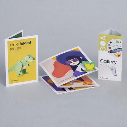 Three colorful folded leaflets and cards are displayed standing and lying on a gray surface.