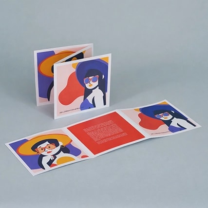 Folded brochure with colourful illustrations of people wearing sunglasses and hats on a gray surface.