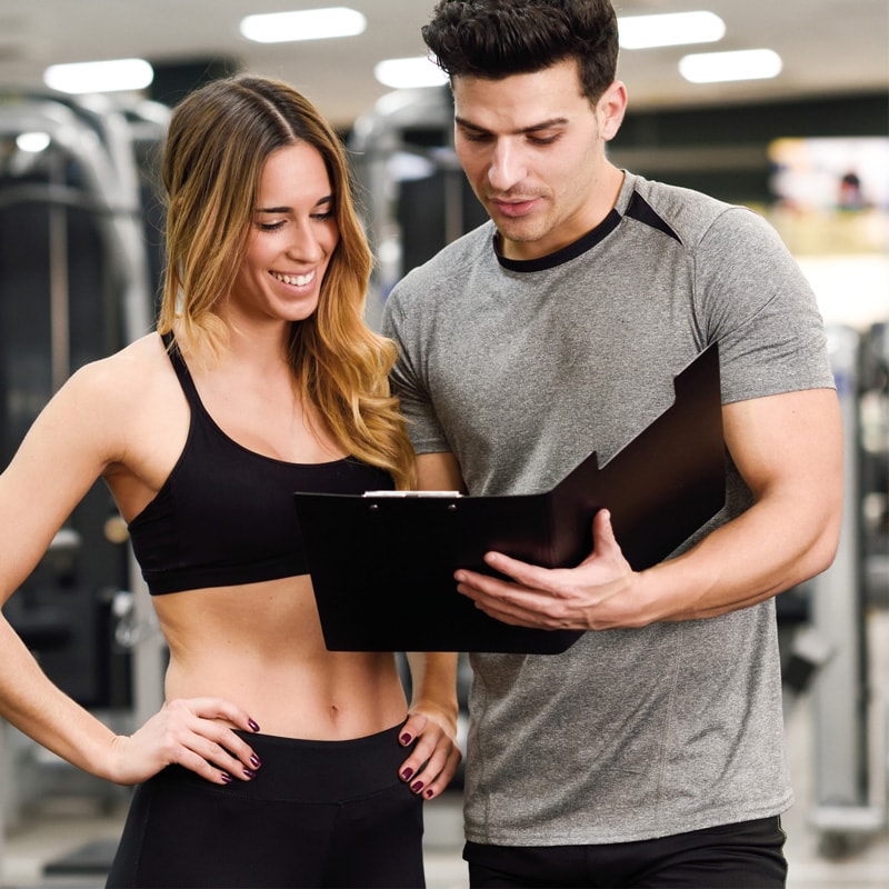A woman and a man review a clipboard together in a gym setting.
