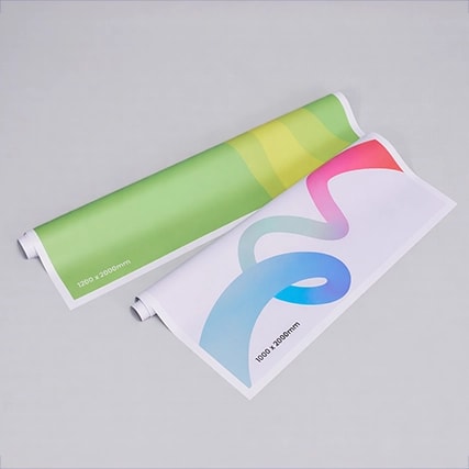 Two rolled posters with colourful abstract designs displayed on a plain gray background.