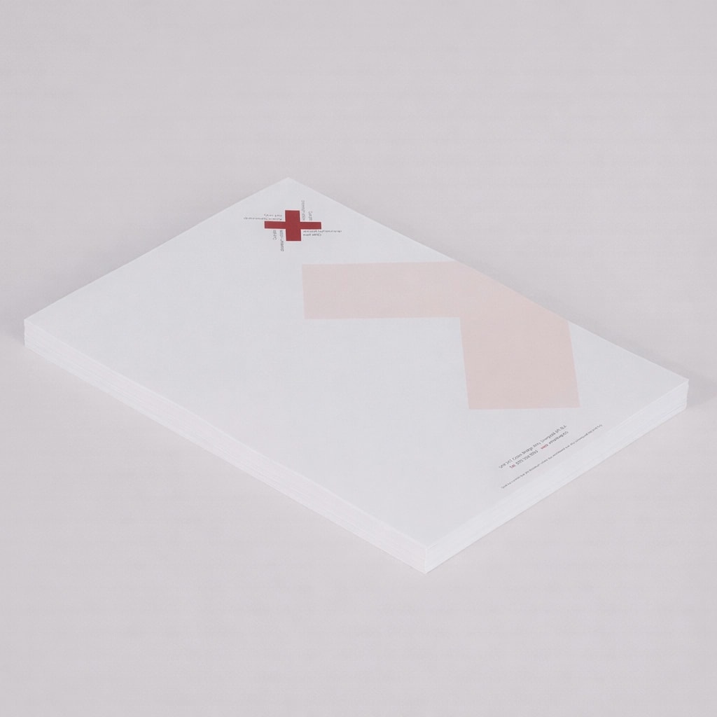 A stack of white letterhead paper with a red cross logo and geometric design in the corner.