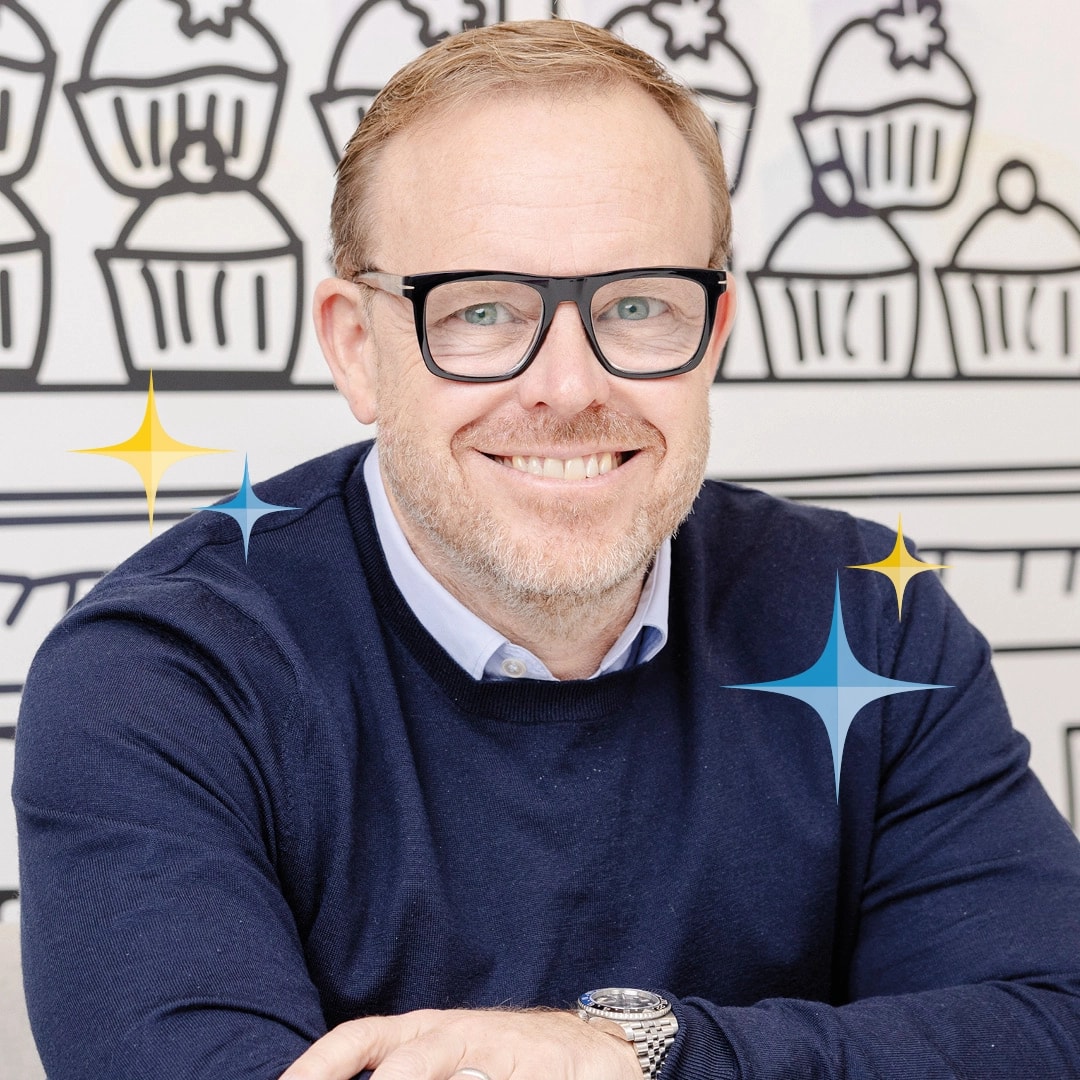Smiling man with glasses in front of cupcake drawings.