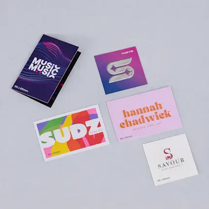 Five colourful custom business cards with various designs and company names displayed on a gray surface.