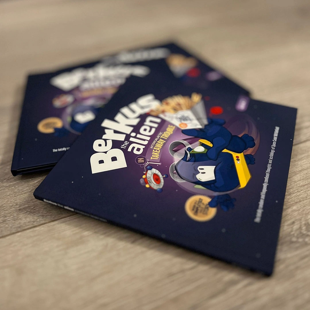 Two illustrated children's books titled "Berkus the Alien" on a wooden surface.