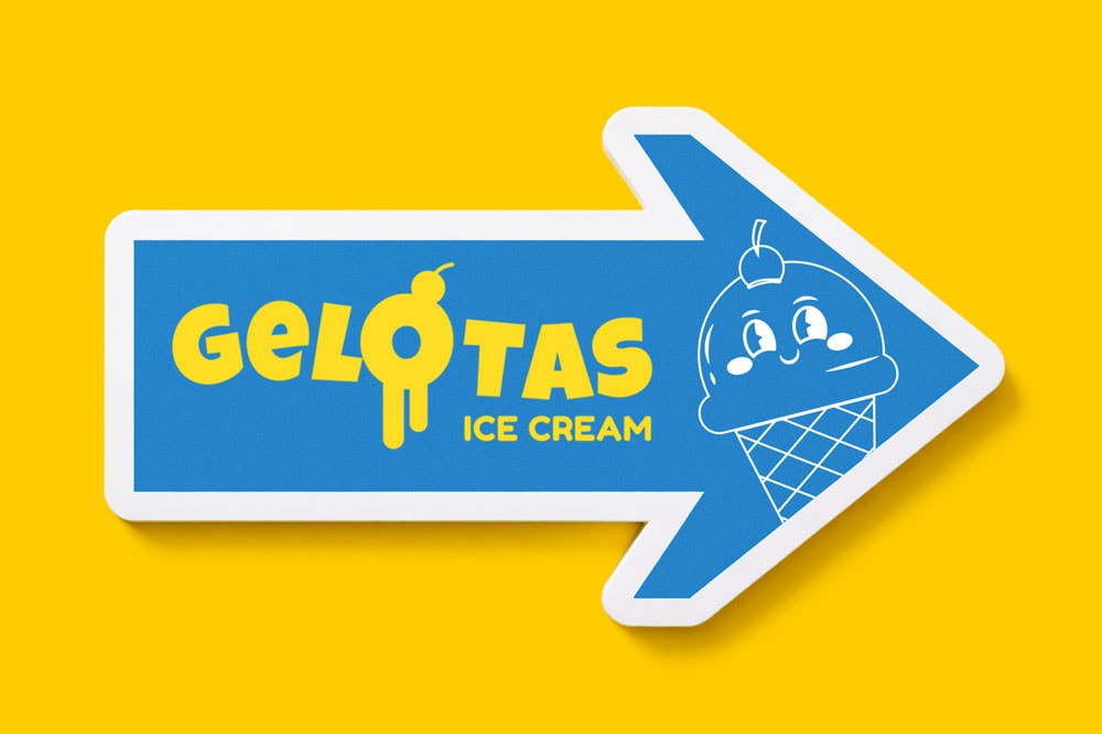 Blue arrow sign with "Gelotas Ice Cream" text and a cartoon ice cream cone on a yellow background.