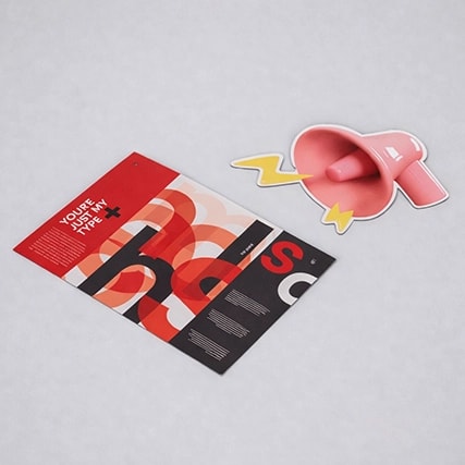 A colourful brochure and a pink megaphone-shaped sticker on a light gray surface.